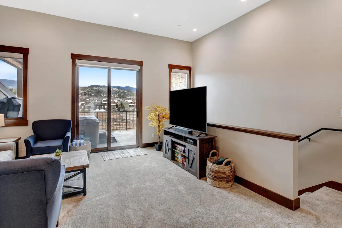 A cozy living area featuring a comfortable armchair, sliding glass doors with sunset views, a modern television, and a decorative plant. The space is set up for both relaxation and entertainment, with natural light creating a welcoming atmosphere.