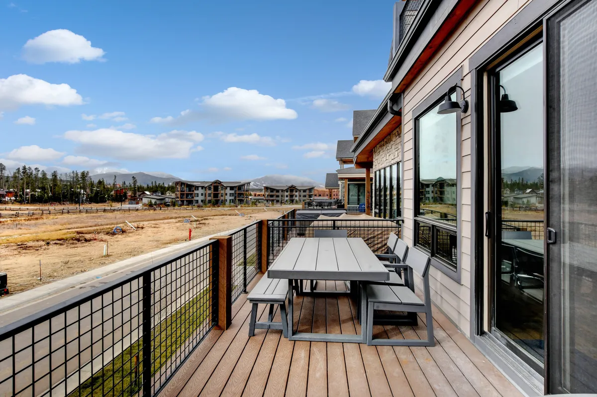 A spacious outdoor deck with comfortable seating overlooks a stunning mountain landscape. Large windows connect the indoor living area to the outdoors, inviting guests to relax after an adventurous day.