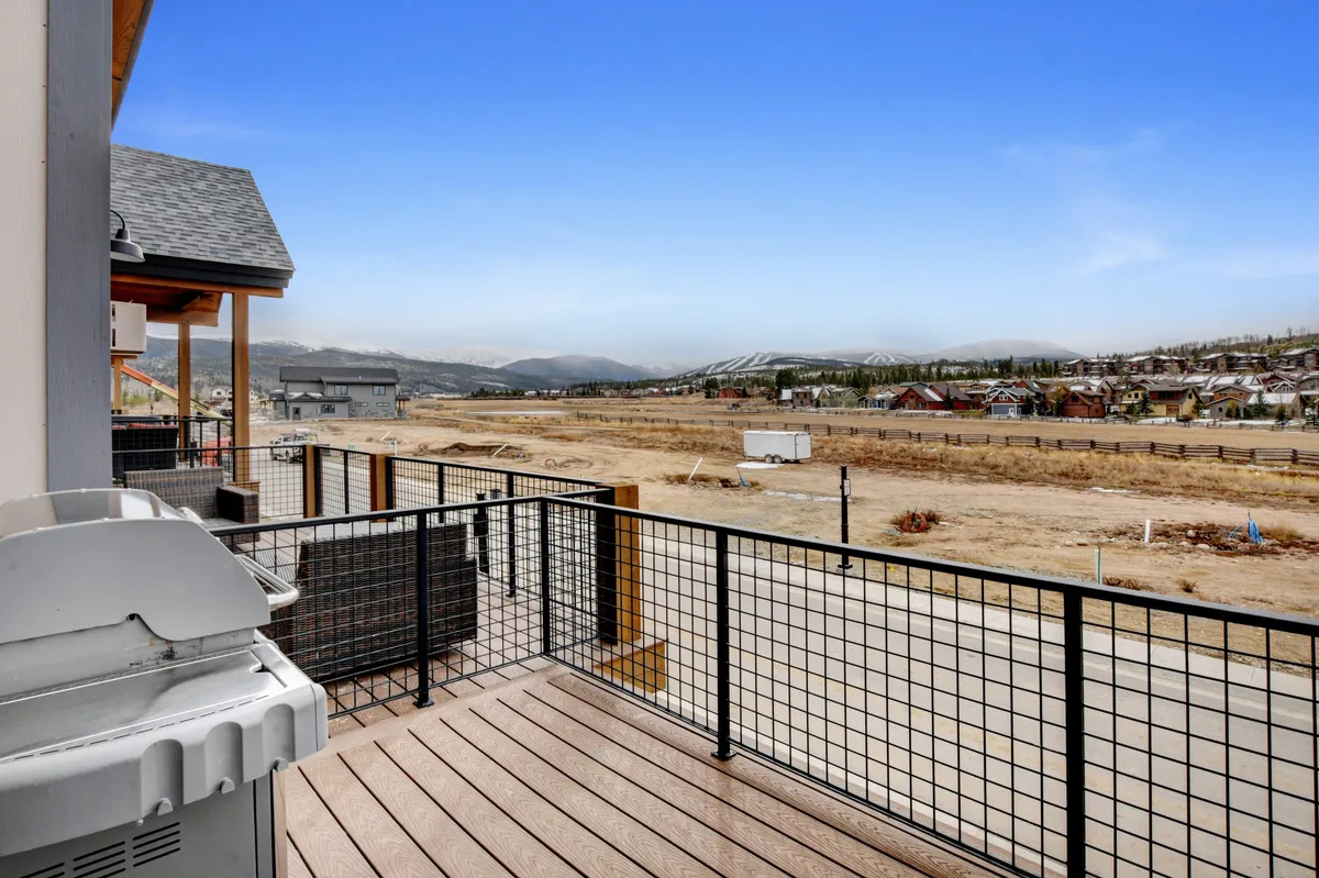 A wide deck featuring a modern BBQ grill, comfortable seating, and expansive views of the surrounding mountains and landscape, ideal for gatherings with friends and family at sunset.