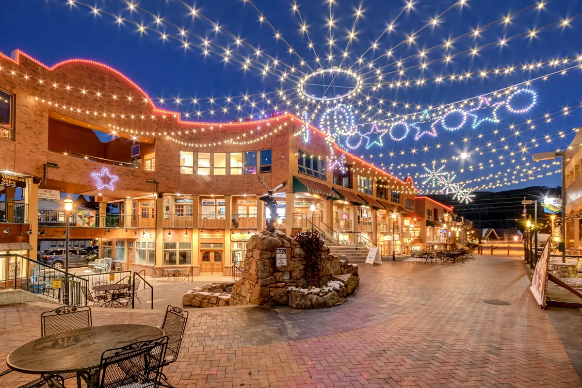 A festive street view with decorative lights, a stone fountain, inviting outdoor seating, and charming shopfronts. The joyful atmosphere suggests seasonal festivities, community gatherings, and a lively downtown perfect for exploring any time of year.