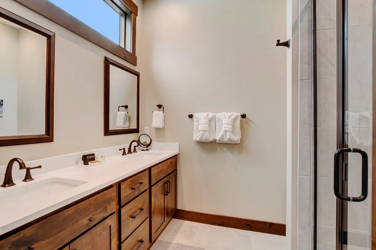 A modern bathroom with dual sinks, large mirrors, and neatly displayed towels. The tranquil environment is perfect for morning routines and self-care, emphasizing luxury and convenience.