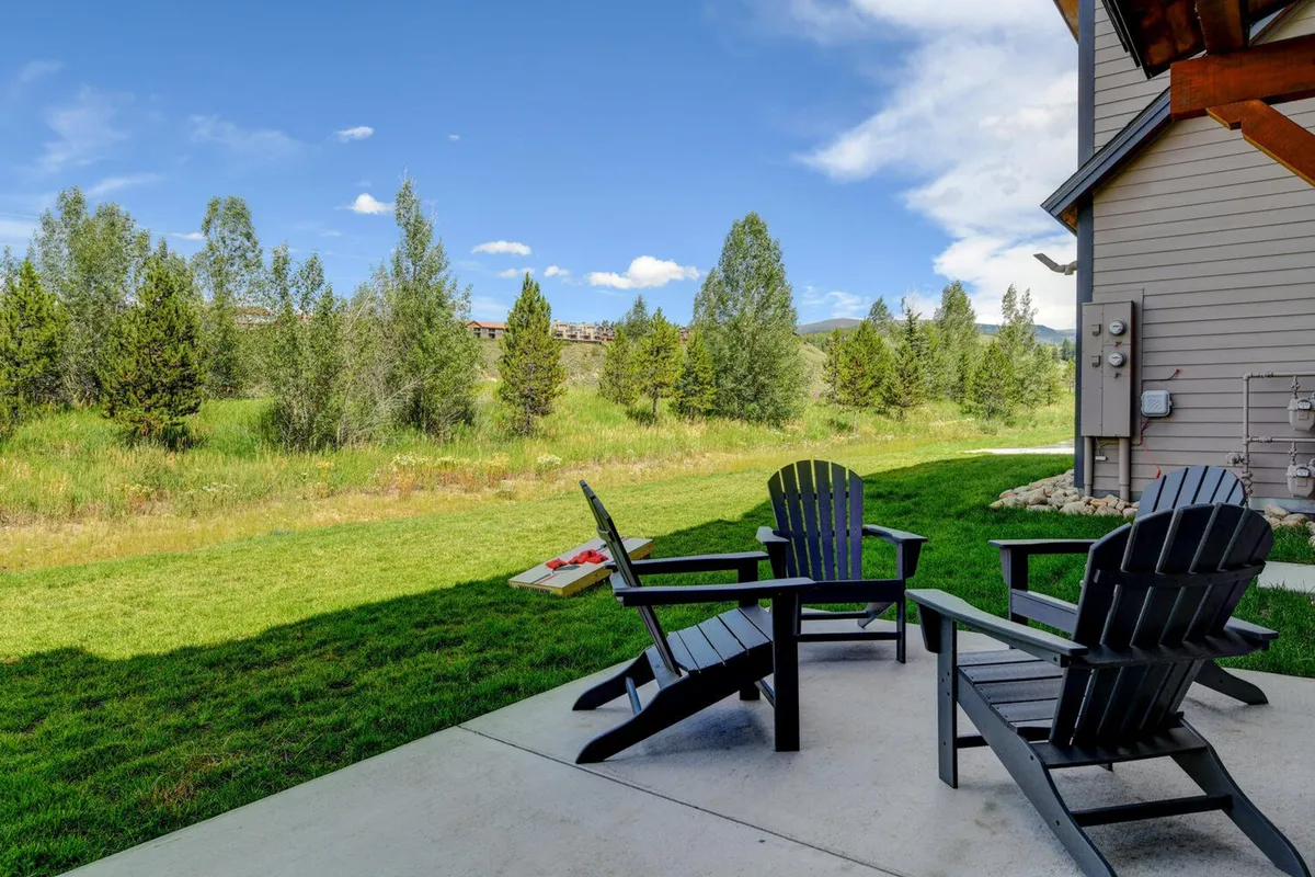 An inviting outdoor setup with Adirondack chairs on a green lawn overlooking distant trees and mountain views. The serene ambiance is perfect for relaxing after a day of mountain activities or for socializing during a summer concert or festival.
