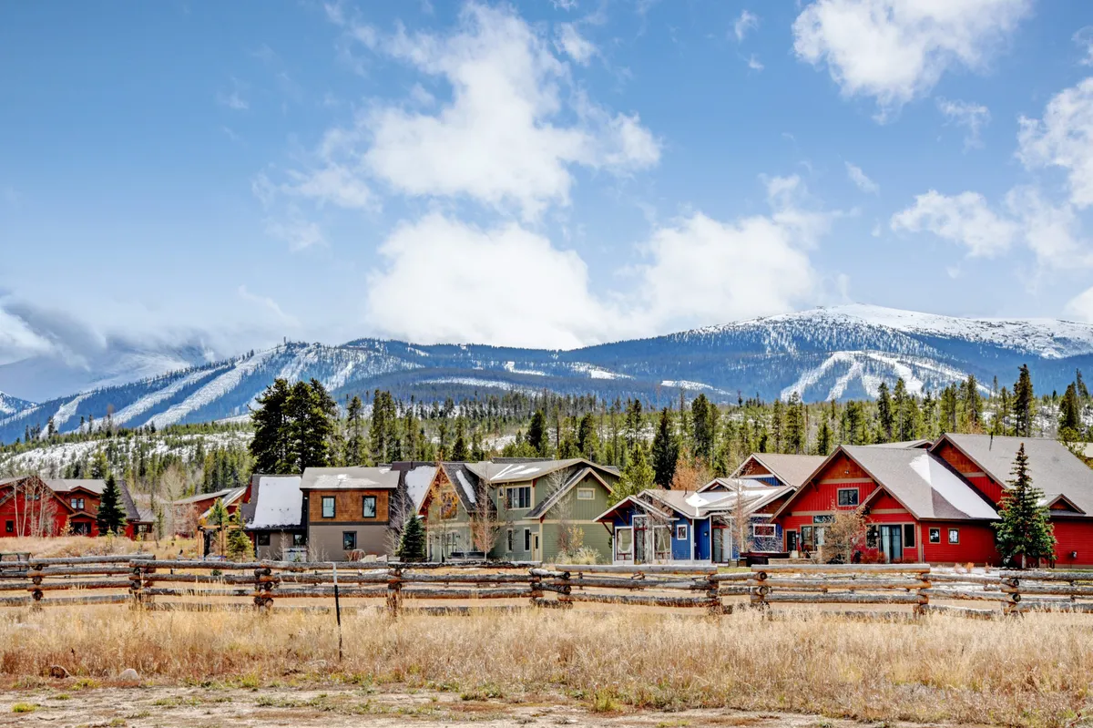 A lively exterior scene featuring colorful houses set against a stunning mountain backdrop, with a fenced area in the foreground. The view suggests opportunities for outdoor activities like hiking, skiing, and local festivals, reflecting the vibrant spirit of Winter Park throughout the year.
