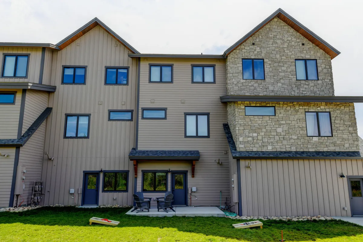 A view of an outdoor patio area featuring comfortable furniture, stone accents, and large windows. The space is perfect for outdoor dining, relaxing in the sun, and social gatherings, with the home's architecture blending seamlessly into the environment.