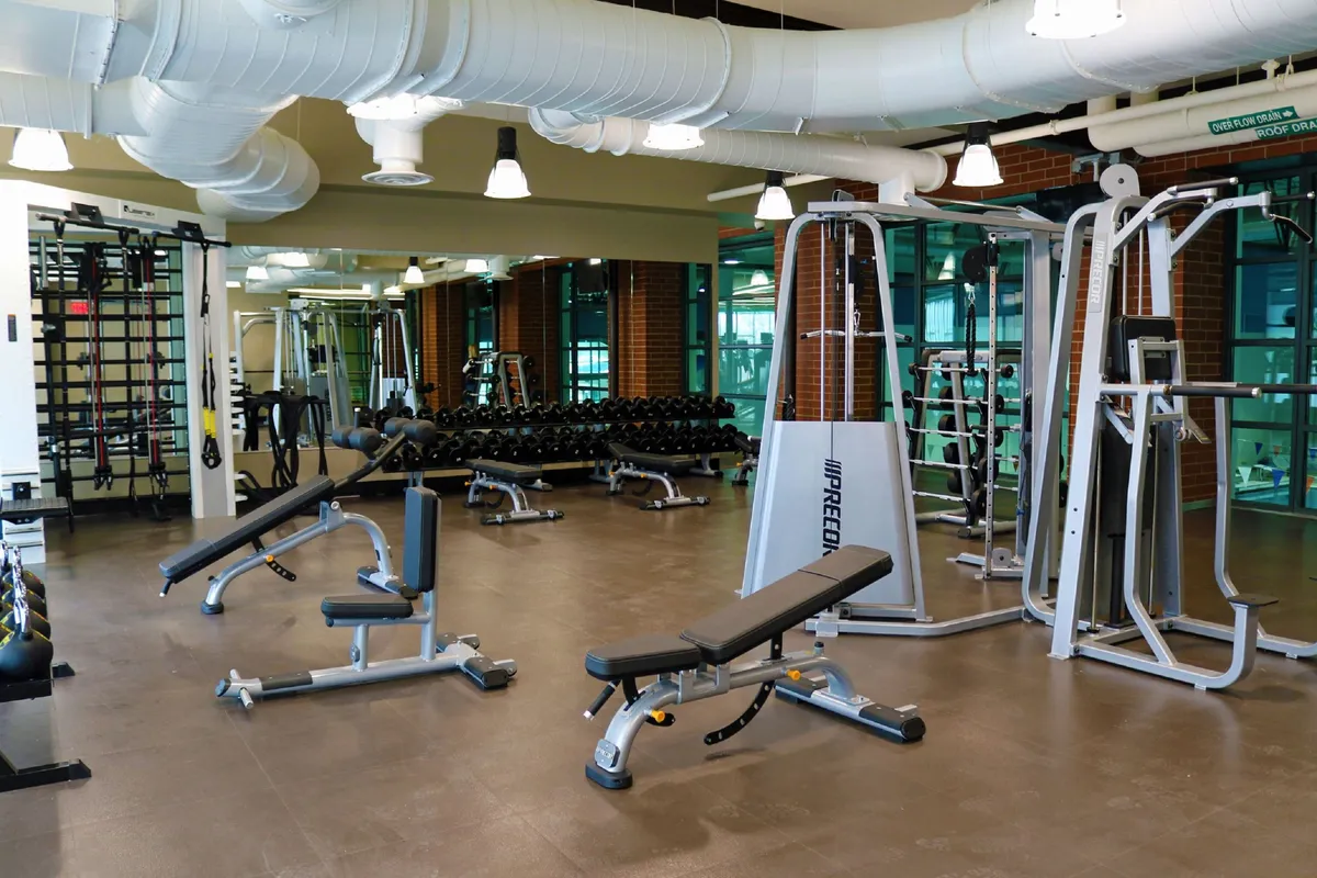 A bright and motivating gym space with weight machines, dumbbell racks, and exercise benches, emphasizing fitness amenities available to guests. The setting is modern and well-equipped, ideal for personal training or group workouts.
