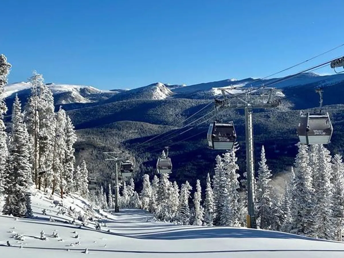 Snow-covered ski lift gondolas glide over a winter landscape of snow-laden trees and dramatic mountain peaks. The scene is adventurous yet serene, conveying the accessibility of world-class skiing and snowboarding just minutes away.