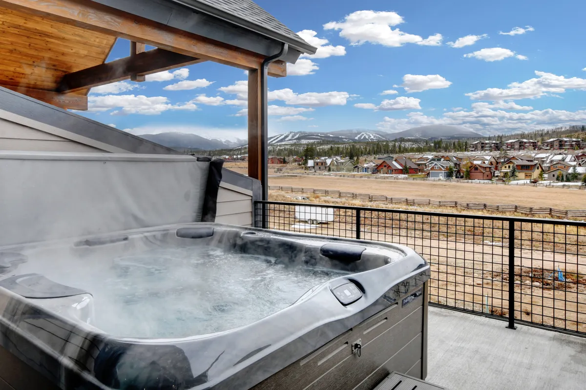 An inviting outdoor hot tub set on a spacious deck, with panoramic mountain views stretching out under the open sky. The setting is serene, perfect for relaxing after a day of adventure or enjoying a soak in the cool mountain air.