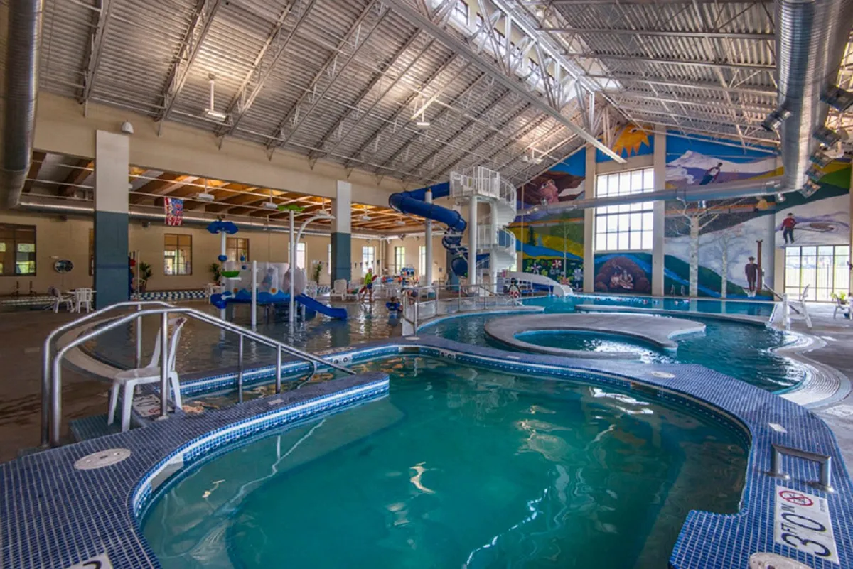 A vibrant indoor recreational center with colorful waterslides, swimming pools, and children playing, conveying the energetic and communal amenities available just a short stroll away.