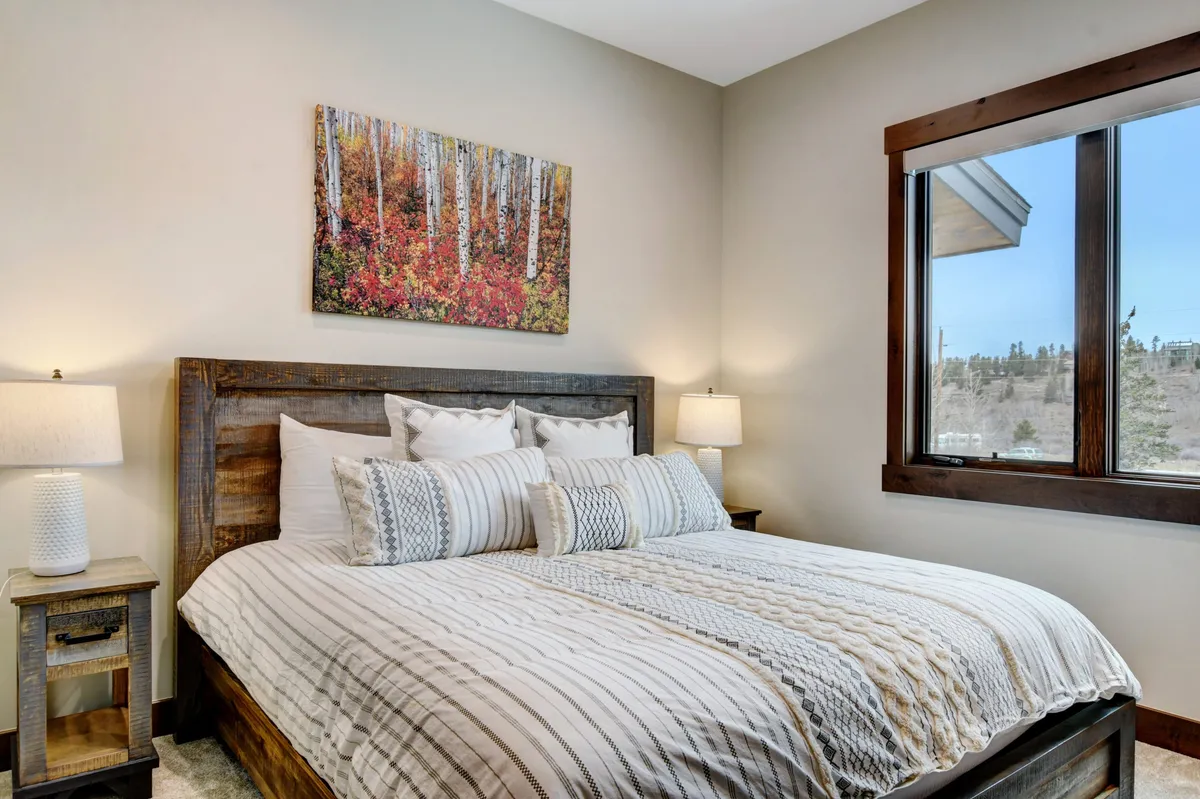 A serene bedroom featuring a comfortable bed, elegant artwork, and a large window that allows natural light to pour in, creating a restful ambiance. The room is furnished for relaxation, inviting guests to unwind in comfort.
